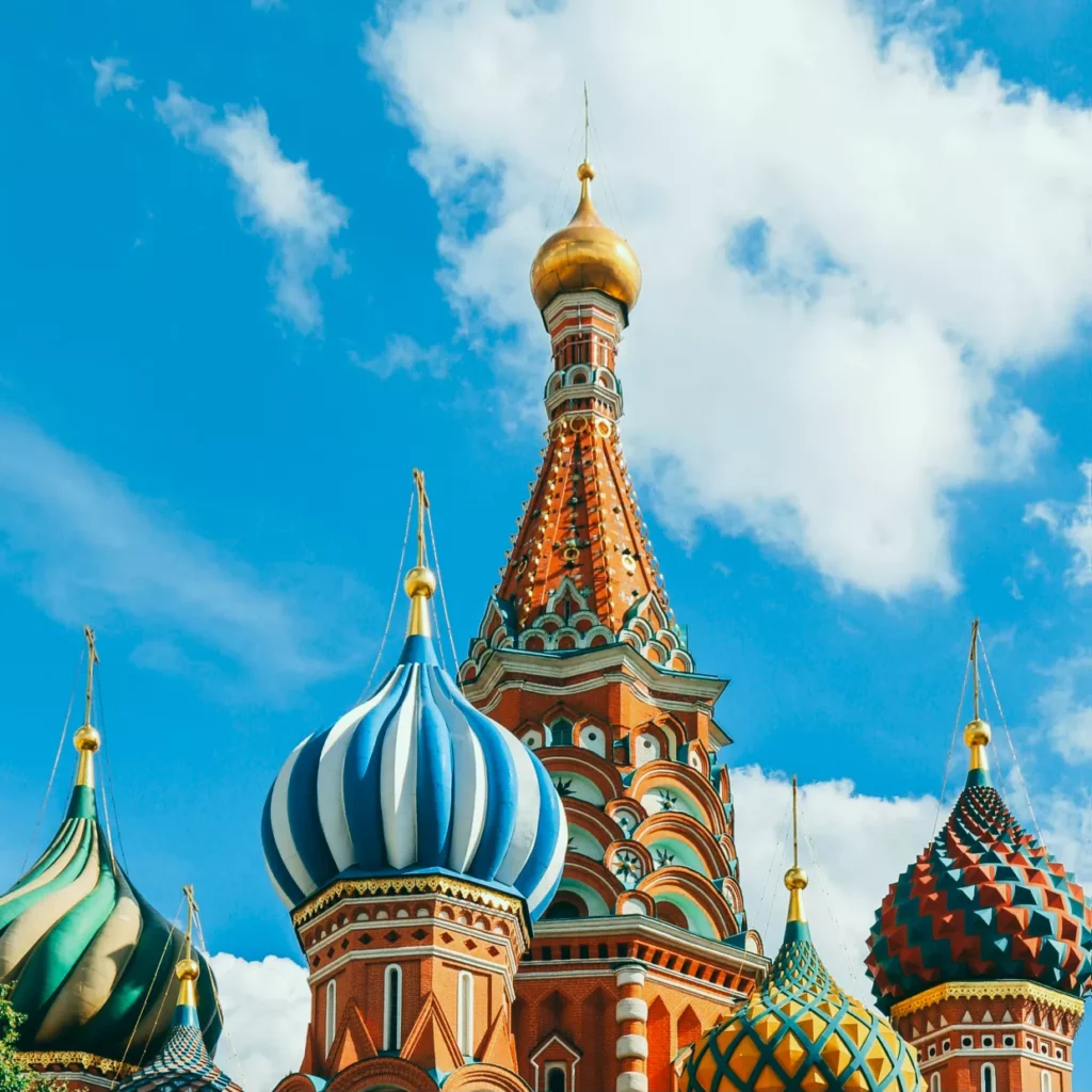 A vibrant image of St. Basil's Cathedral in Moscow, Russia. The building features colorful onion-shaped domes in bright patterns and intricate designs, set against a clear blue sky with a few clouds. This is on our Russia work permit guide.